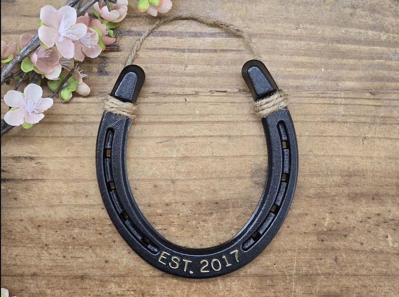 Real horseshoe painted an oil-rubbed bronze color and engraved with a last name and date. Jute string attached at the top for hanging.