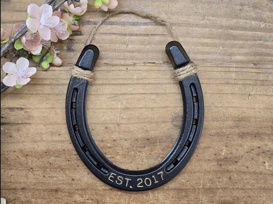 Real horseshoe painted an oil-rubbed bronze color and engraved with a last name and date. Jute string attached at the top for hanging.