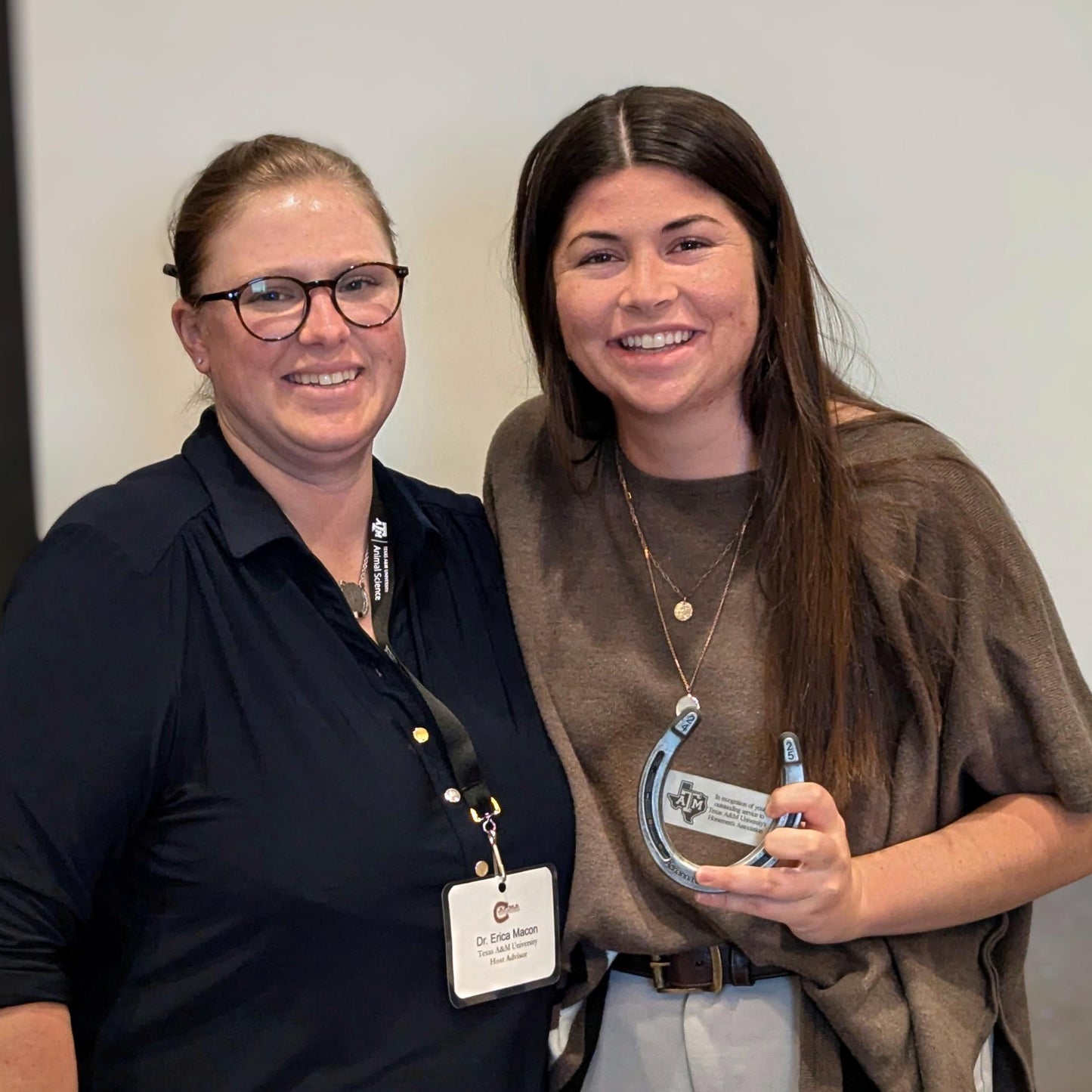A student posting with her teacher holding the custom horseshoe award she was presented.