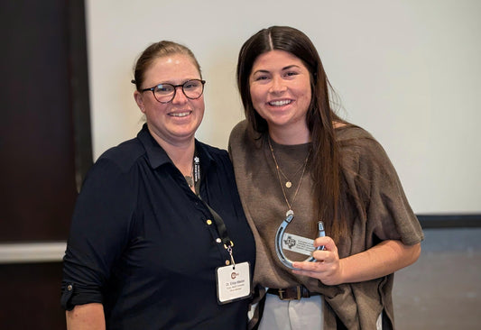 A student posting with her teacher holding the custom horseshoe award she was presented.
