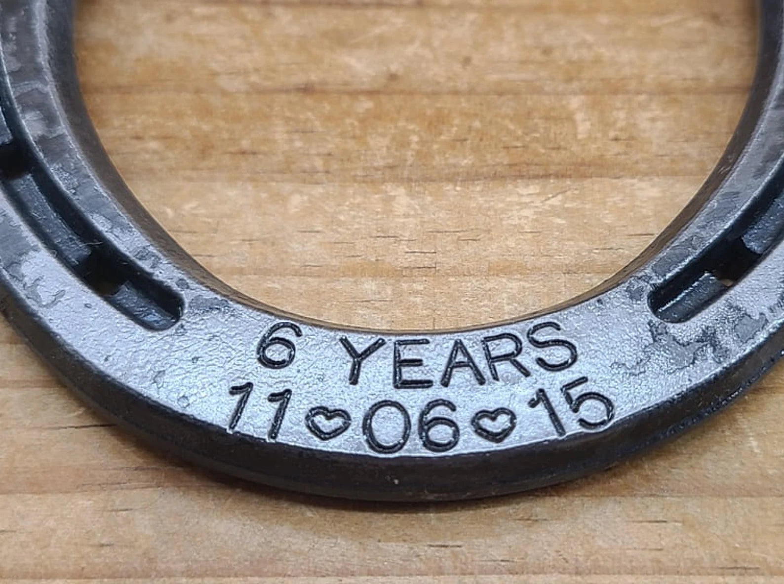 Close up view of a real horseshoe engraved with '6 YEARS' plus an anniversary date along the bottom toe portion of the horseshoe.