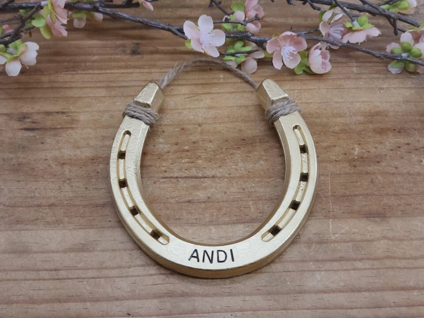 Real horseshoe painted gold and personalized with a name along the bottom. Jute string attached at the top for hanging.