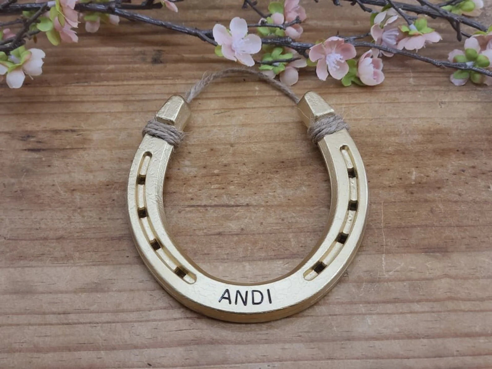 Real horseshoe painted gold and personalized with a name along the bottom. Jute string attached at the top for hanging.