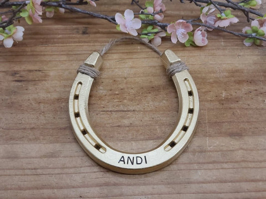 Real horseshoe painted gold and personalized with a name along the bottom. Jute string attached at the top for hanging.