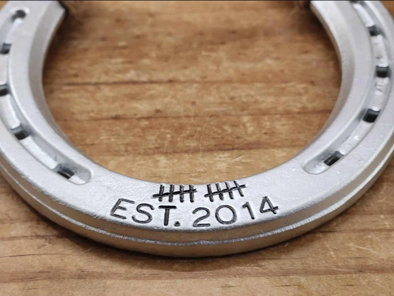 Close up photo of a personalized aluminium painted horseshoe with 10 tally marks and 'EST. 2014' engraving along the bottom and jute twine accents, perfect as a rustic 10 year anniversary gift or home decor piece.