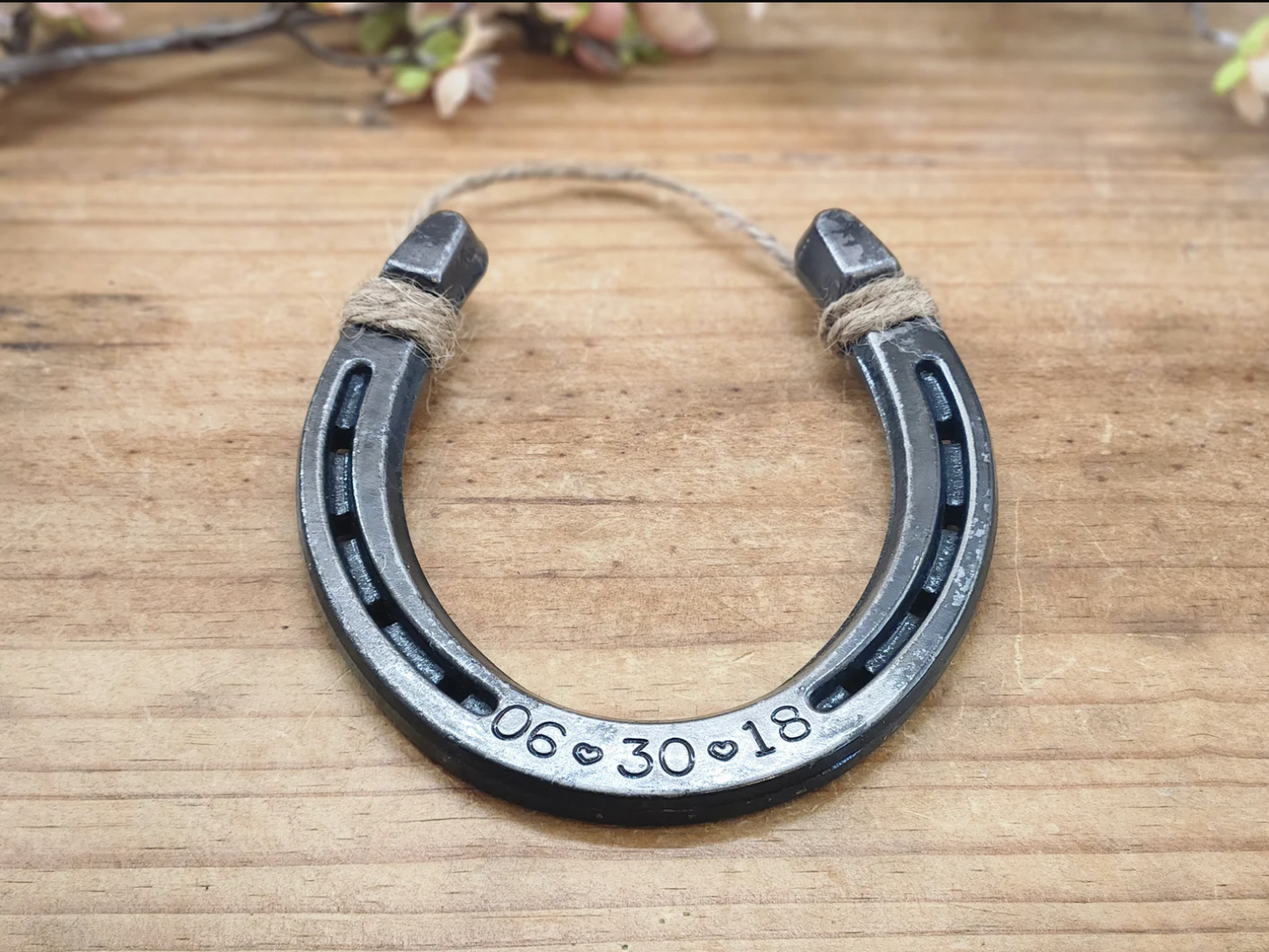 Real horseshoe engraved with anniversary date along the bottom. Date is formatted with numbers and hearts in between the month, day and year. Jute string attached at the top for hanging.