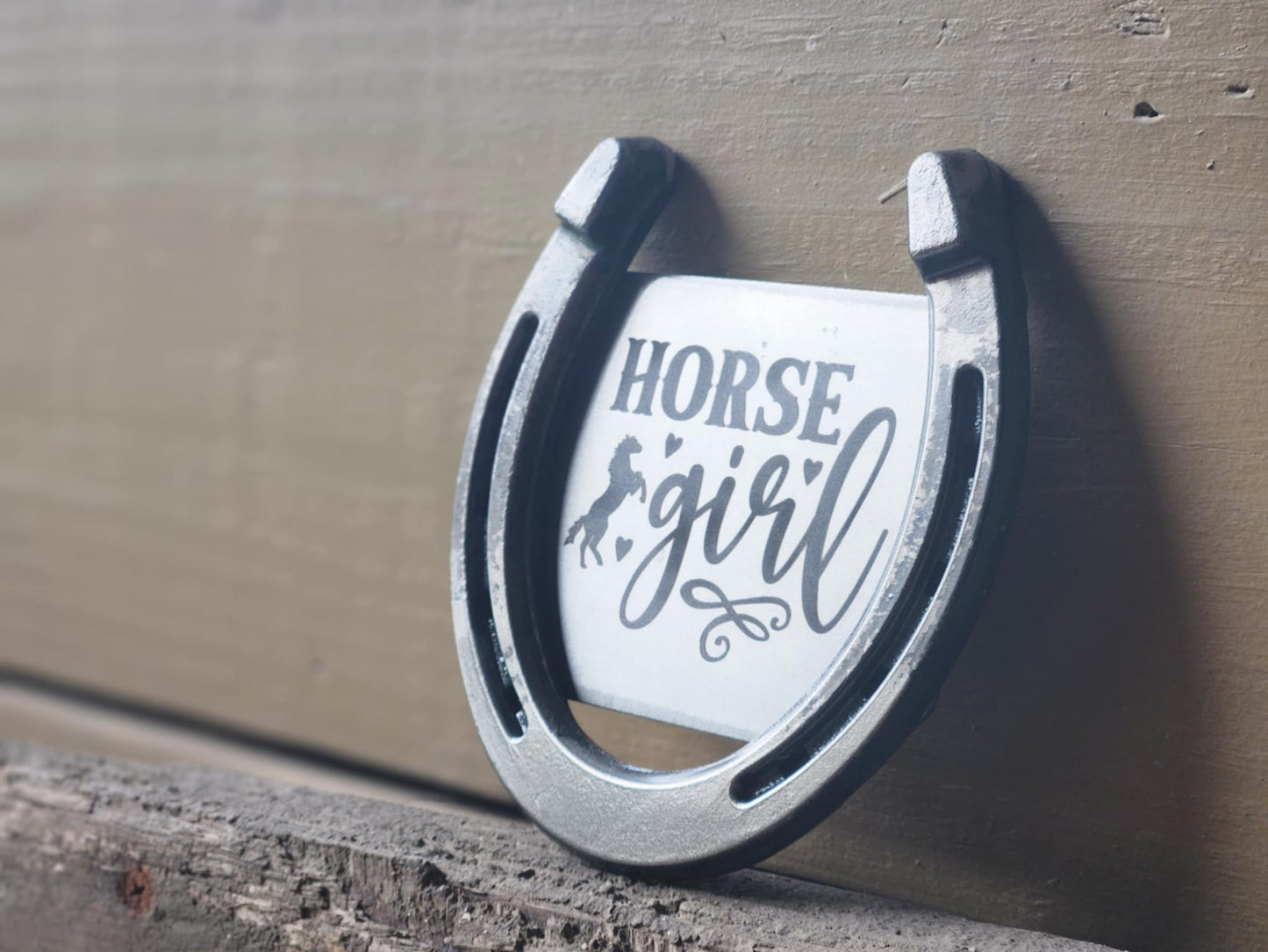 Outdoor photo of a real horseshoe with "Horse Girl' text, a horse and hearts engraved on the center.