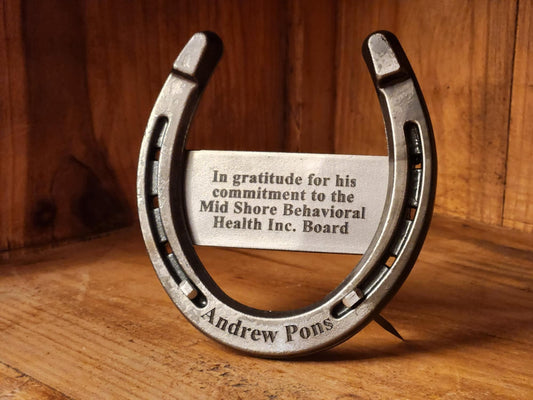 Real horseshoe displayed free-standing on a shelf. Engraved with a special message on a metal plaque and the person's name along the bottom. 