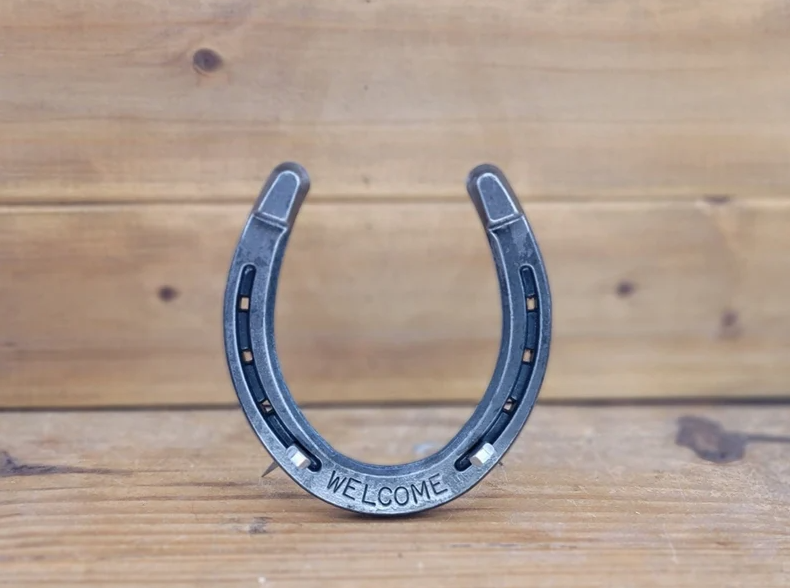 Real horseshoe with the word 'WELCOME' stamped along the bottom. Shown freestanding with horseshoe nails supporting the bottom.