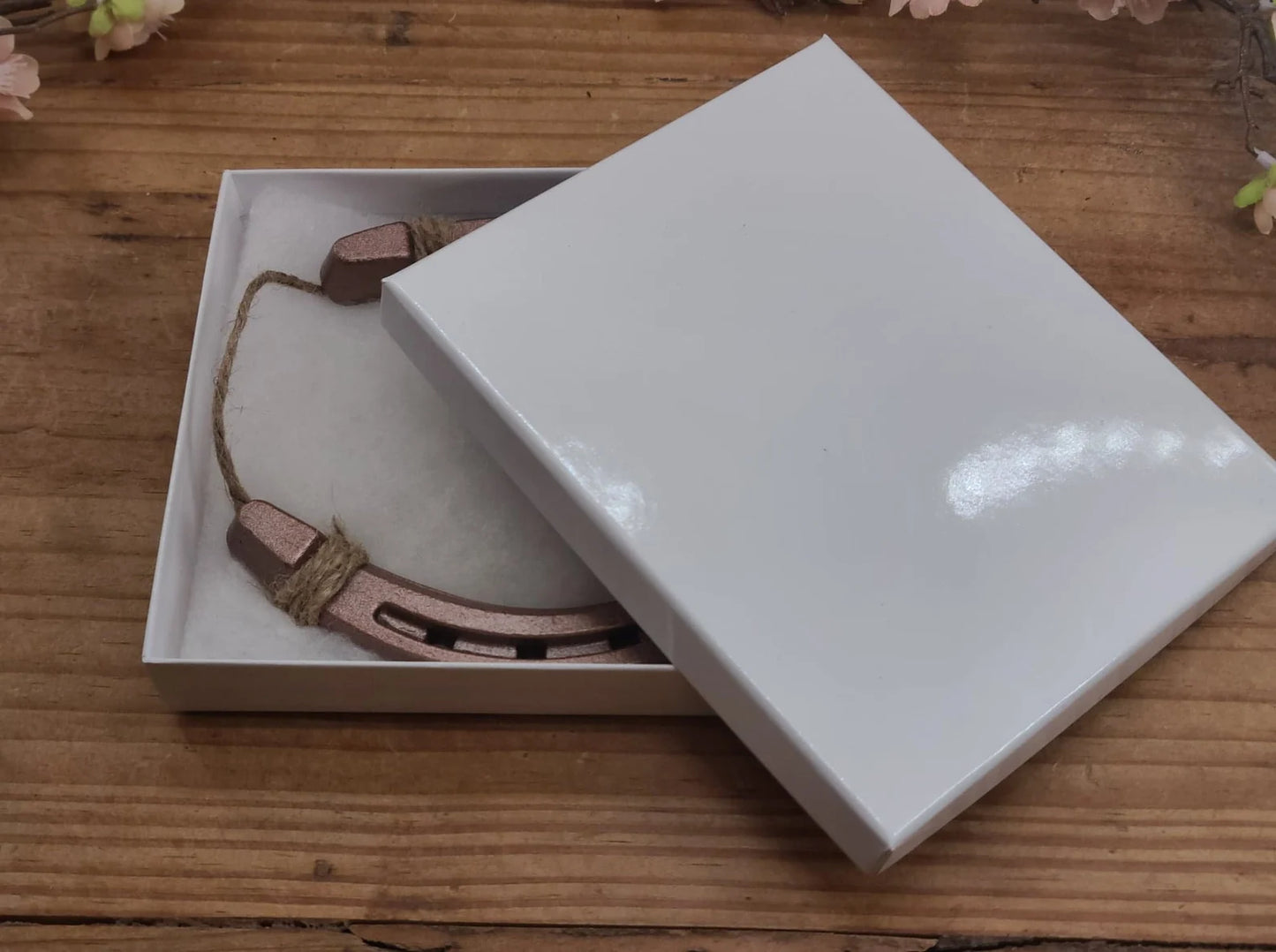 Single copper colored horseshoe shown in a plain white gift box