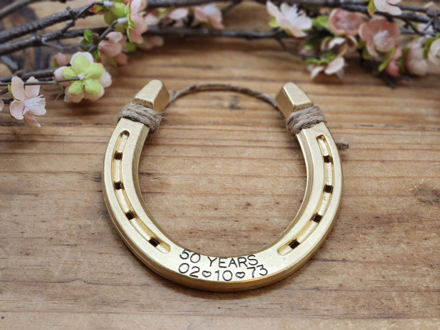 Real horseshoe painted gold and stamped along the bottom with the words '50 YEARS' plus an anniversary date. Jute string tied at the top of the horseshoe for hanging.