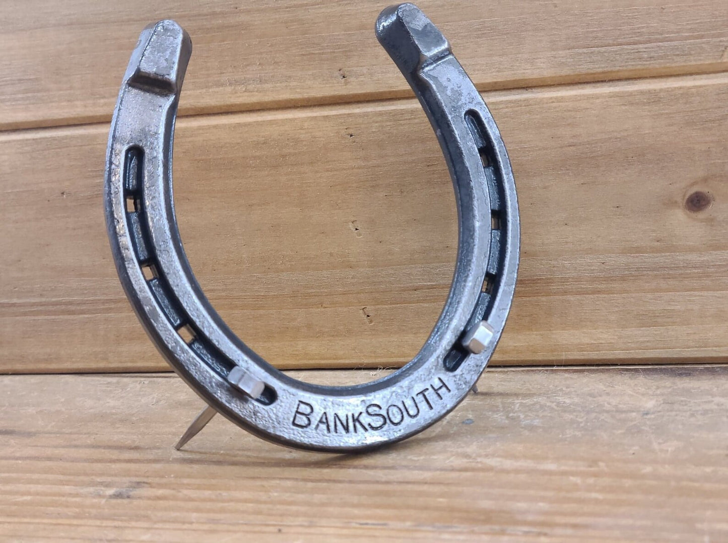 Real horseshoe with a word stamped along the bottom and displayed freestanding with horseshoe nails for support.