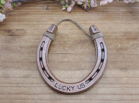 Real horseshoe painted copper with the words 'LUCKY US' stamped along the bottom and the year in the upper corners of the horseshoe.