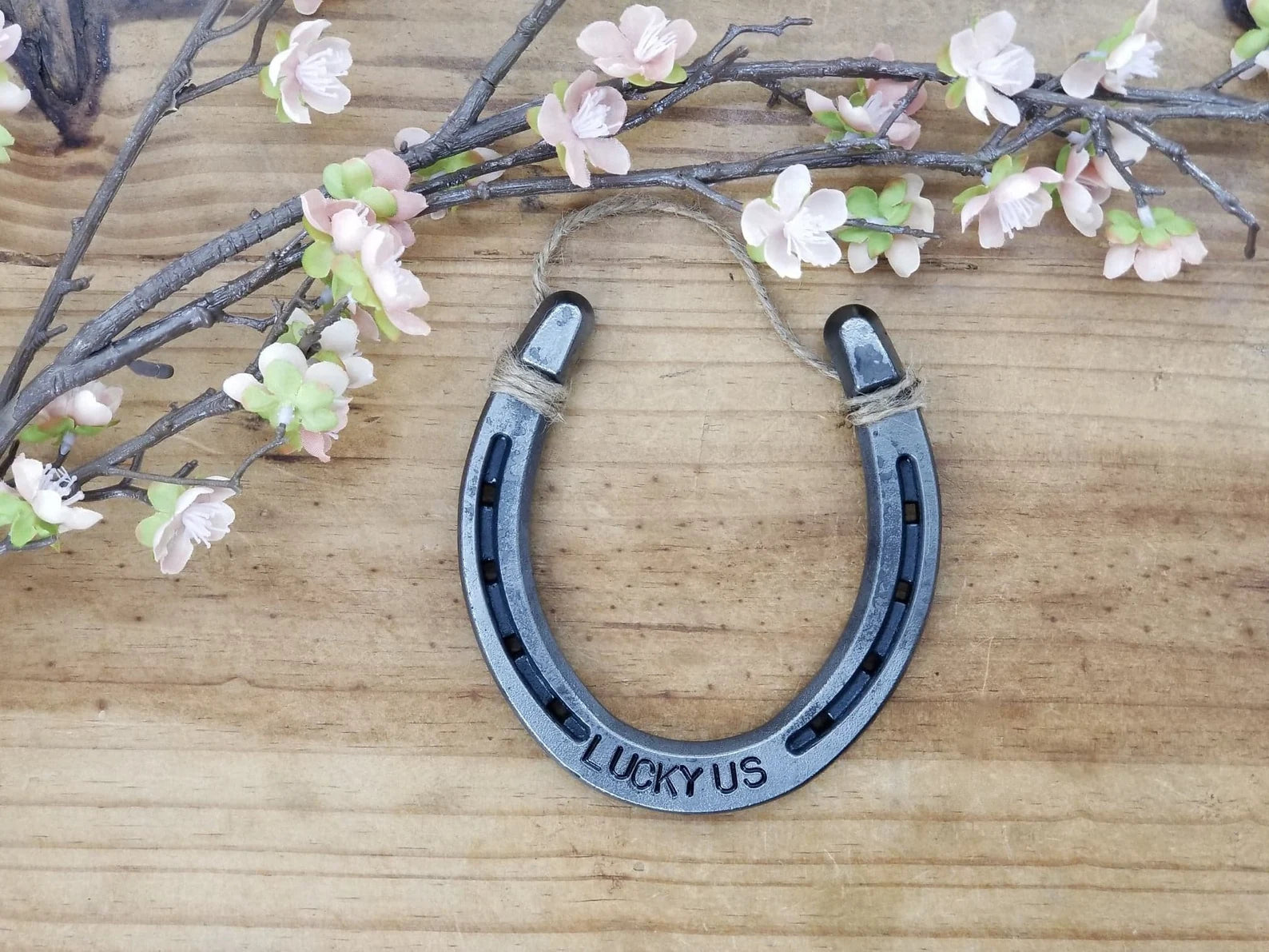 Real horseshoe stamped with the words 'LUCKY US' along the bottom. Jute string at the top of the horseshoe for hanging.