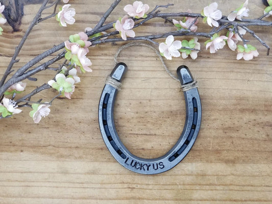 Real horseshoe stamped with the words 'LUCKY US' along the bottom. Jute string at the top of the horseshoe for hanging.