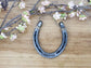 Real horseshoe stamped with the words 'LUCKY US' along the bottom. Jute string at the top of the horseshoe for hanging.