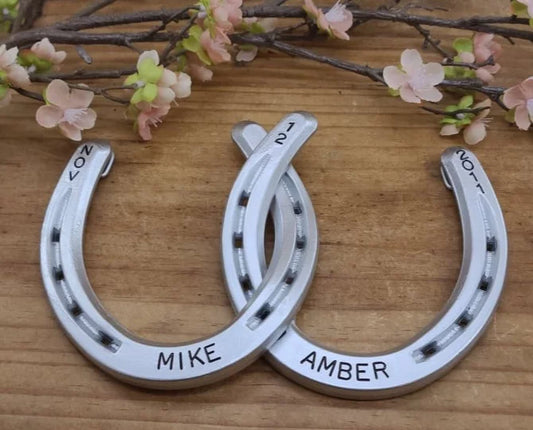 Real horseshoes painted aluminum color and welded together. Personalized with names along the bottom and date at the top. Designed to hang on a wall.