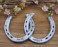 Real horseshoes painted aluminum color and welded together. Personalized with names along the bottom and date at the top. Designed to hang on a wall.
