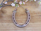 Real horseshoe painted copper with two lines of personalization. Pictured with a last name and a date stamped along the bottom of the horseshoe.